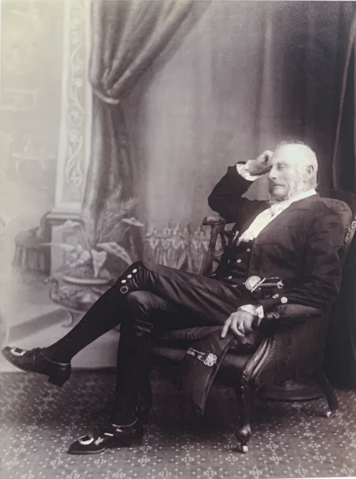 Man wearing black tail coat, jabot, breeches, silver buckled shoes